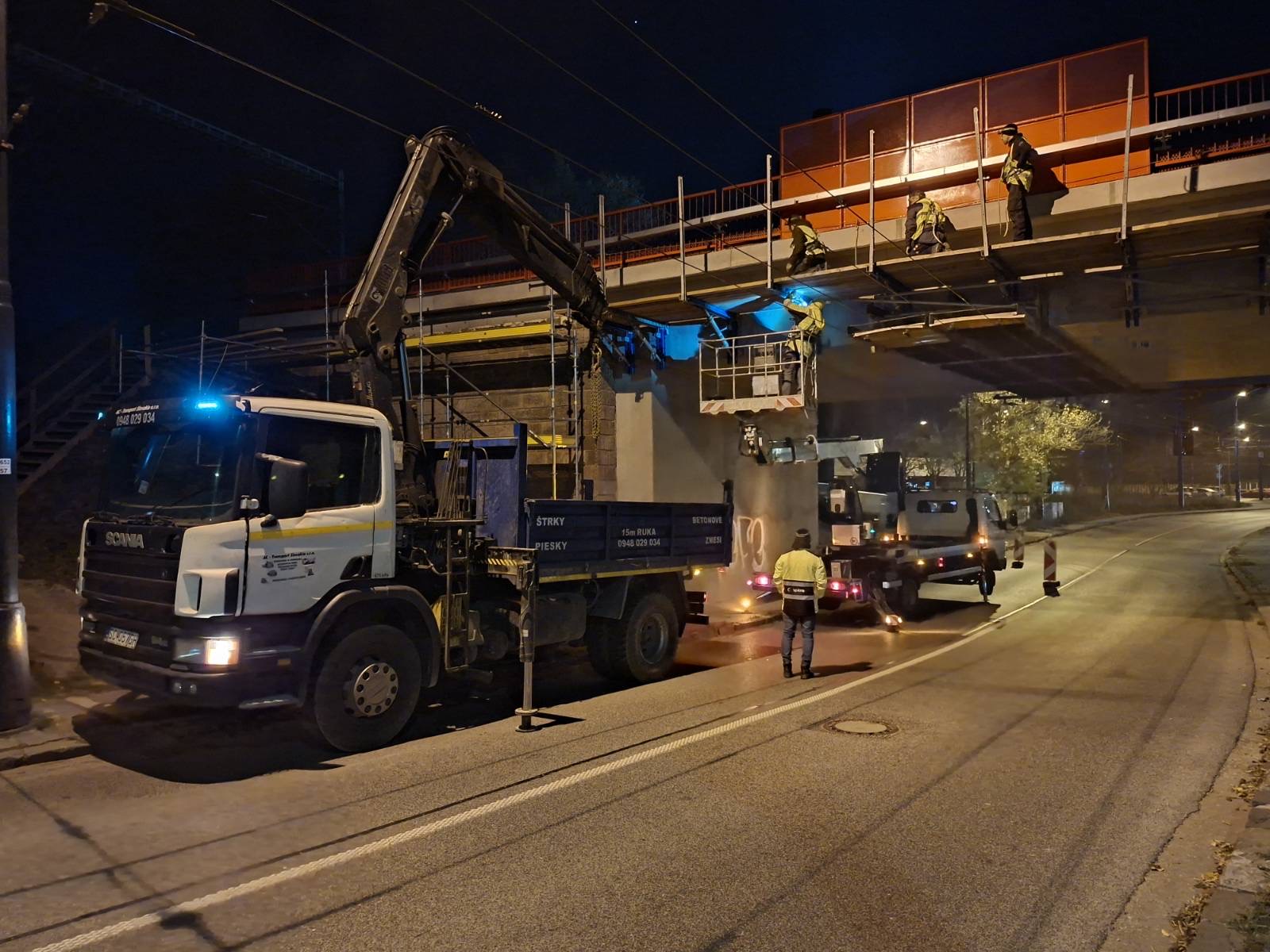 Nákladné auto s hydraulickou rukou pracuje v noci pri moste.